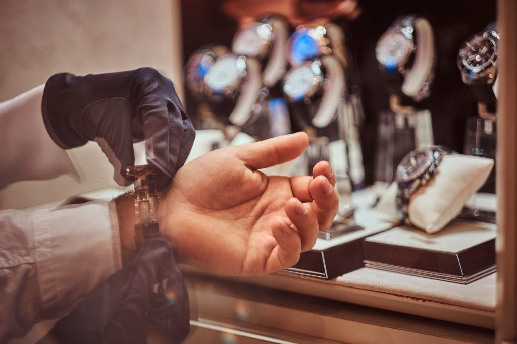 Close-up hands. Assistant helps the client to try on exclusive men's watches.
