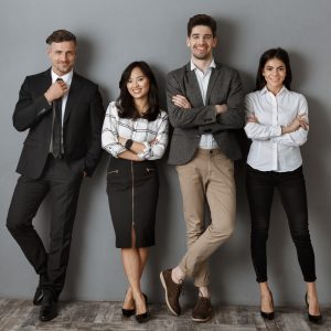 smiling multicultural business people in formal wear standing at grey wall