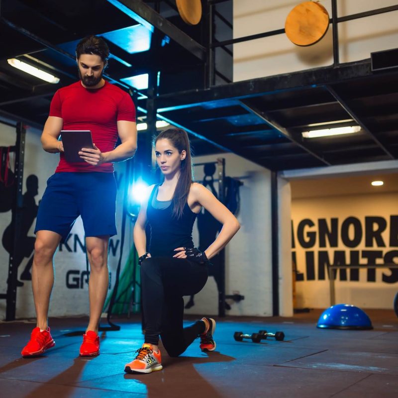 gym-instructor-assisting-two-sporty-women-with-squats-in-fitness-center-