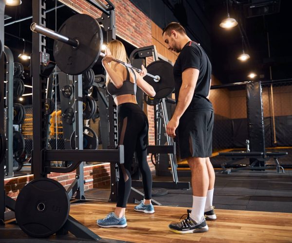 professional-gym-instructor-assisting-woman-at-the-gym