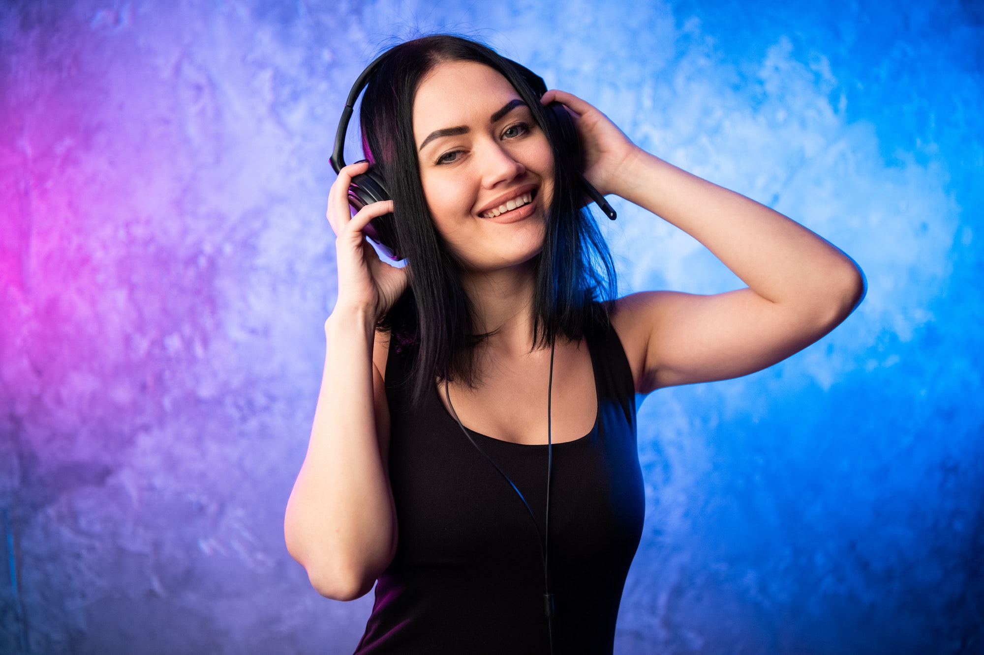 Colorful portrait in blue and pink ligth of a young DJ woman wearing headset and enjoying an